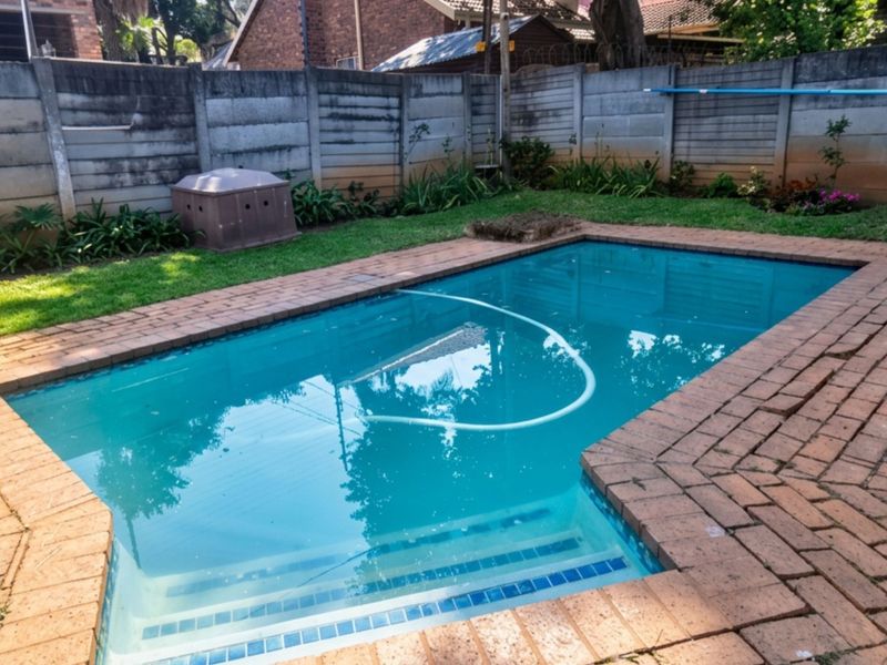 A backyard swimming pool area featuring brick paving and a surrounding precast concrete boundary wall.