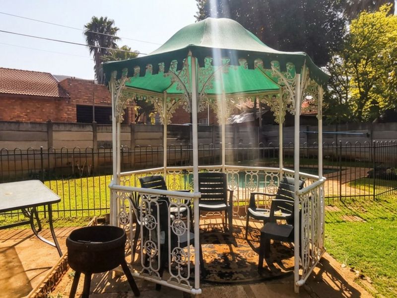 A backyard garden area featuring a wrought iron gazebo, a swimming pool, and secure perimeter fencing.