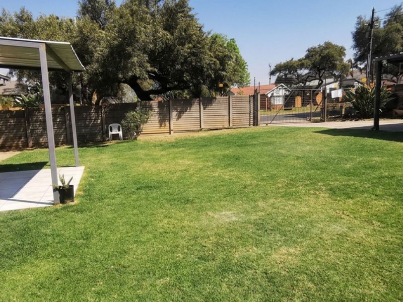 Spacious rear garden featuring a covered patio with tiled flooring, brick exterior walls, and a detached carport structure.