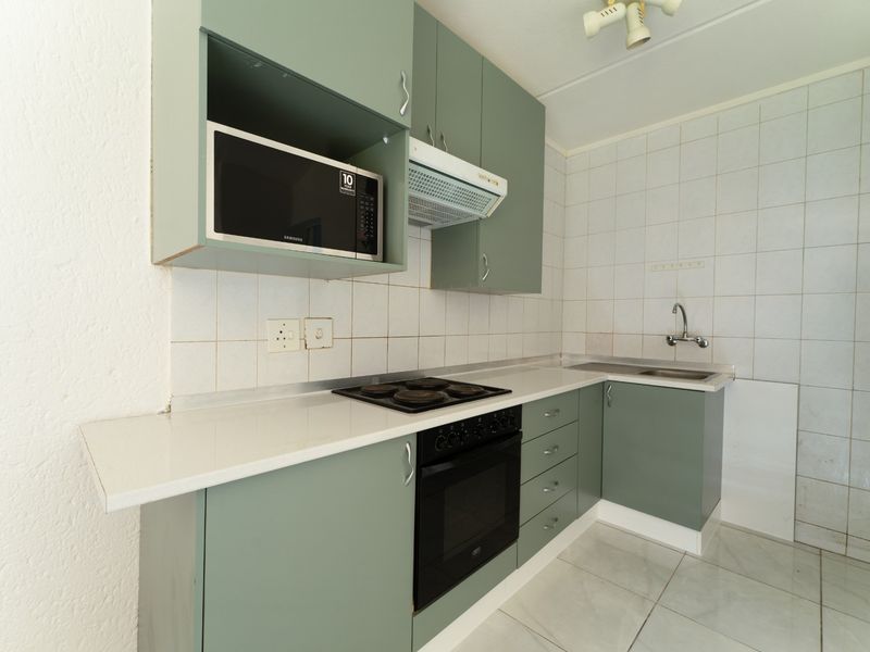 A functional kitchen featuring sage green cabinetry, built-in oven and hob, extractor fan, and tiled splashbacks with a clean, neutral layout.