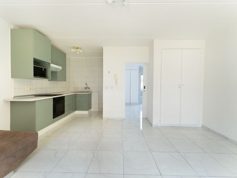 Open-plan living area featuring a functional kitchen with built-in cabinetry, oven, hob, and tiled flooring throughout.
