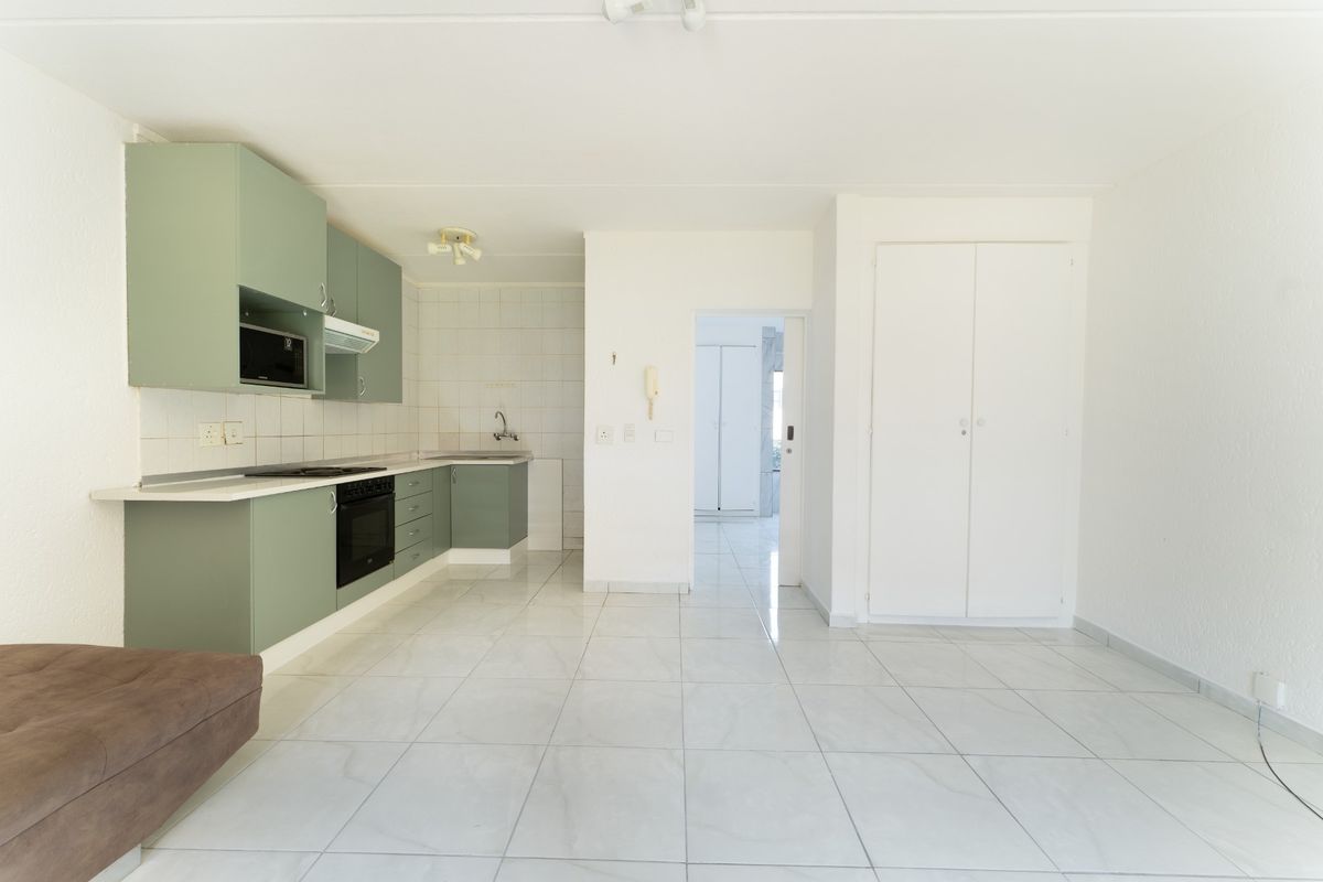 Open-plan living area featuring a functional kitchen with built-in cabinetry, oven, hob, and tiled flooring throughout.