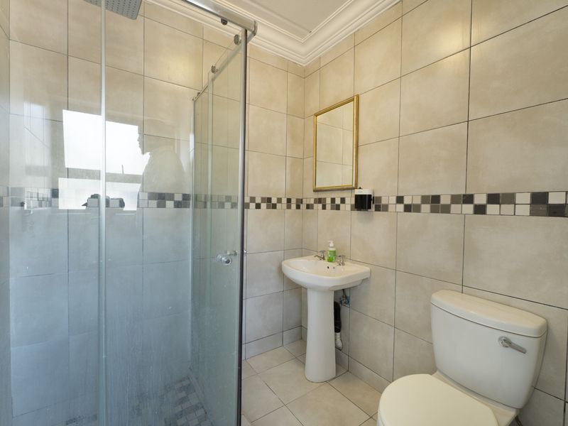 A functional bathroom featuring a pedestal basin, toilet, and a glass-enclosed shower with neutral wall and floor tiling.