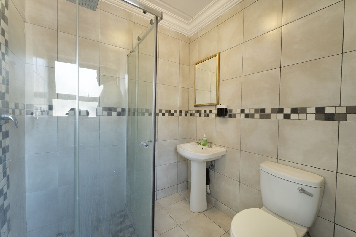 A functional bathroom featuring a pedestal basin, toilet, and a glass-enclosed shower with neutral wall and floor tiling.