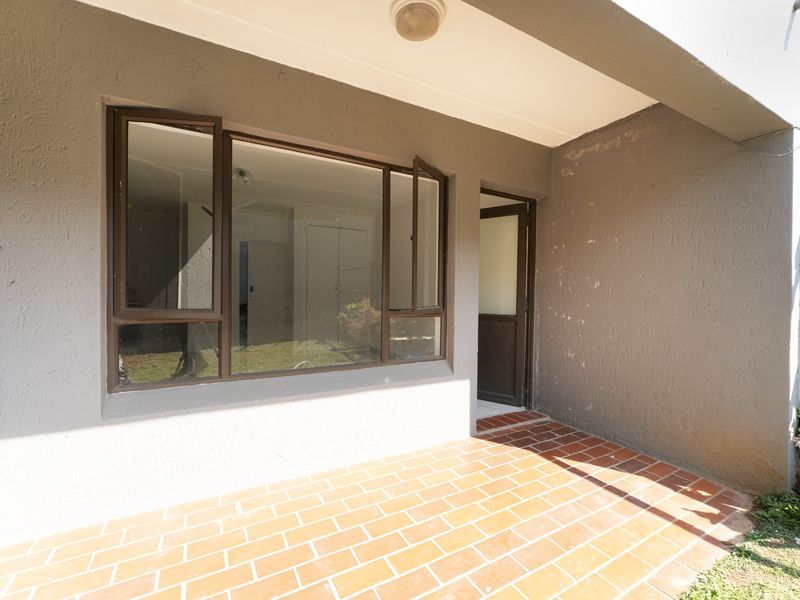 A covered patio area featuring terracotta tiled flooring, aluminium window and door frames, and textured exterior walls in need of minor maintenance.