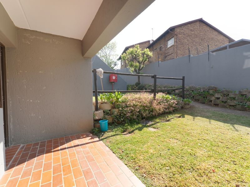 A private ground floor patio area featuring brick paving, a small lawn, and a retaining wall with a timber fence boundary.