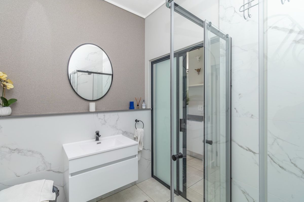 Modern bathroom featuring a wall-mounted vanity with basin, marble-look wall tiles, and a glass shower enclosure with a sliding door.