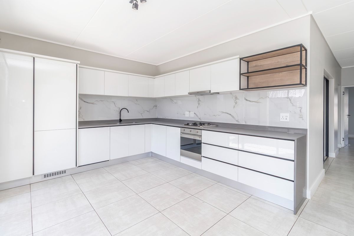 Modern kitchen featuring sleek white cabinetry, stone countertops, marble-look splashback, integrated oven, gas hob, and high-quality tiled flooring.