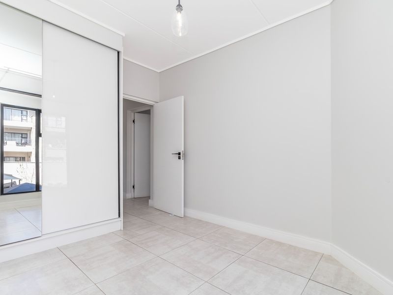 A bright, empty bedroom featuring neutral tiled flooring, a built-in wardrobe with mirrored sliding doors, and clean white finishes.