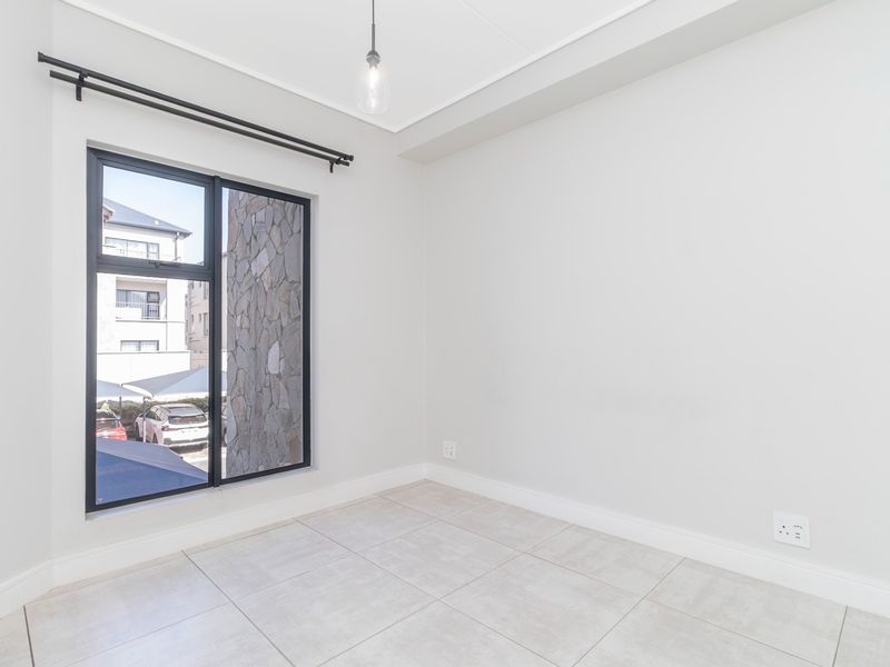 A bright, empty bedroom featuring neutral tiled flooring, clean white walls, and a large window with a black frame.