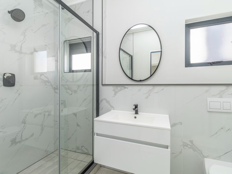 Modern bathroom featuring a walk-in shower with glass enclosure, wall-mounted vanity with basin, and contemporary marble-look wall tiling.