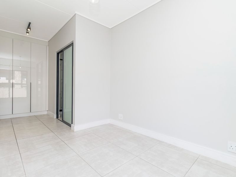 A bright, empty bedroom featuring modern tiled flooring, built-in cupboards, and a sliding door leading to an adjacent space.