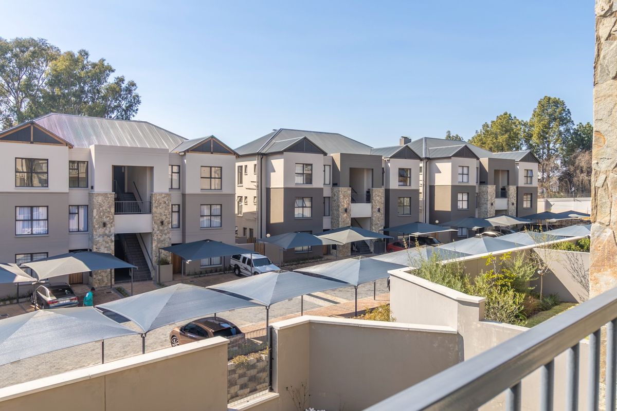 Elevated view of a modern apartment complex featuring multi-story buildings with stone accents, metal roofing, and designated shade cloth parking bays.