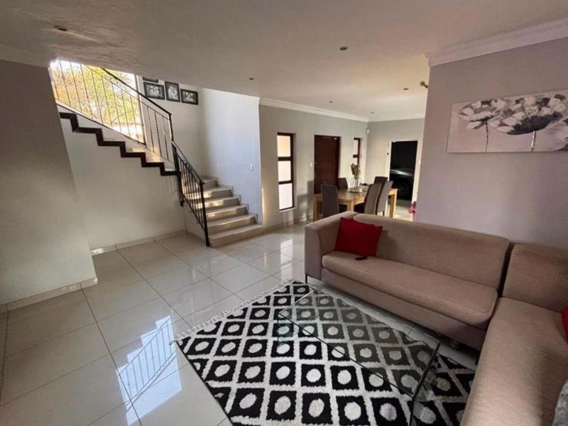 Spacious open-plan living area featuring tiled flooring, a central staircase with metal balustrades, and recessed lighting throughout the main living and dining space.