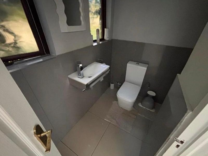 A compact, modern guest bathroom featuring tiled walls, a wall-mounted basin with chrome fixtures, and a standard toilet.