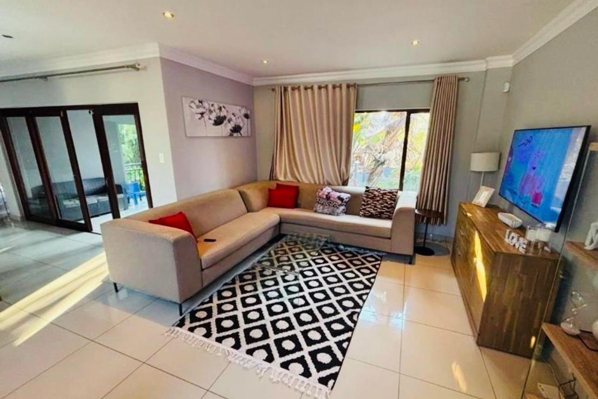 A well-lit living room featuring large format floor tiles, recessed downlighting, and sliding glass doors leading to an outdoor area.