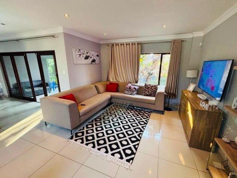 A well-lit living room featuring large format floor tiles, recessed downlighting, and sliding glass doors leading to an outdoor area.