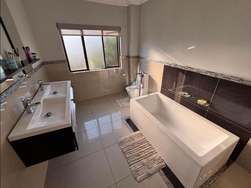 Modern bathroom featuring a double vanity, built-in bathtub, and bidet with neutral wall and floor tiling.