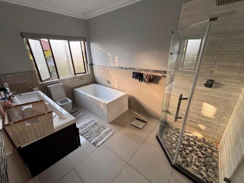 Modern bathroom featuring a glass-enclosed shower with pebble flooring, a built-in bathtub, and a vanity cabinet with neutral wall tiling.