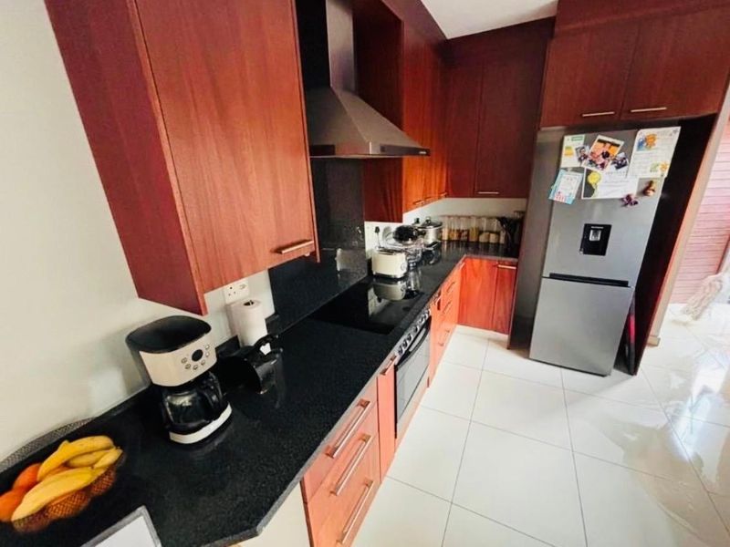 A functional kitchen featuring dark wood cabinetry, black granite countertops, built-in oven, electric cooktop, and stainless steel extractor fan with tiled flooring.