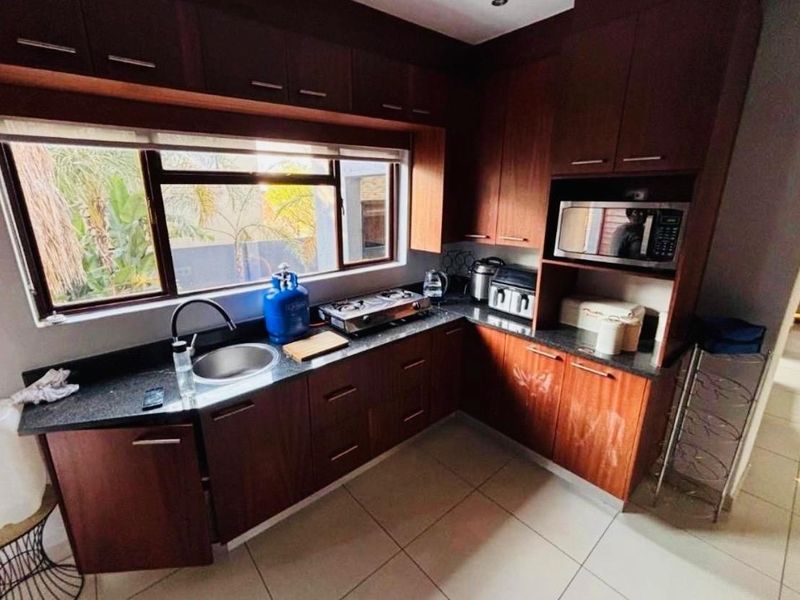 A functional kitchen featuring dark wood cabinetry, granite countertops, a stainless steel sink, and built-in microwave space with tiled flooring.