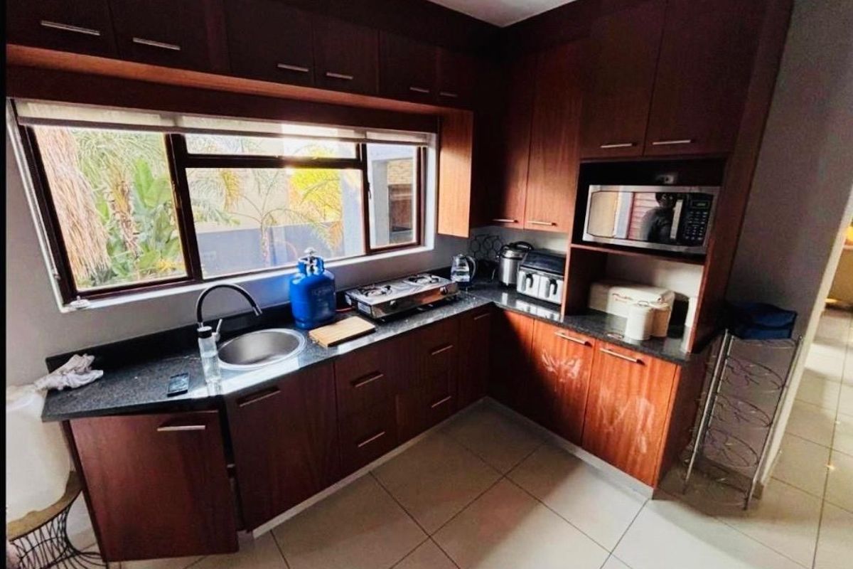 A functional kitchen featuring dark wood cabinetry, granite countertops, a stainless steel sink, and built-in microwave space with tiled flooring.