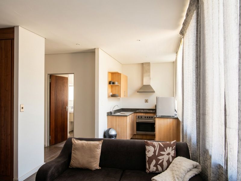 Open-plan living area featuring a compact kitchen with built-in cabinetry, granite countertops, stainless steel oven, and extractor fan, leading to a hallway.
