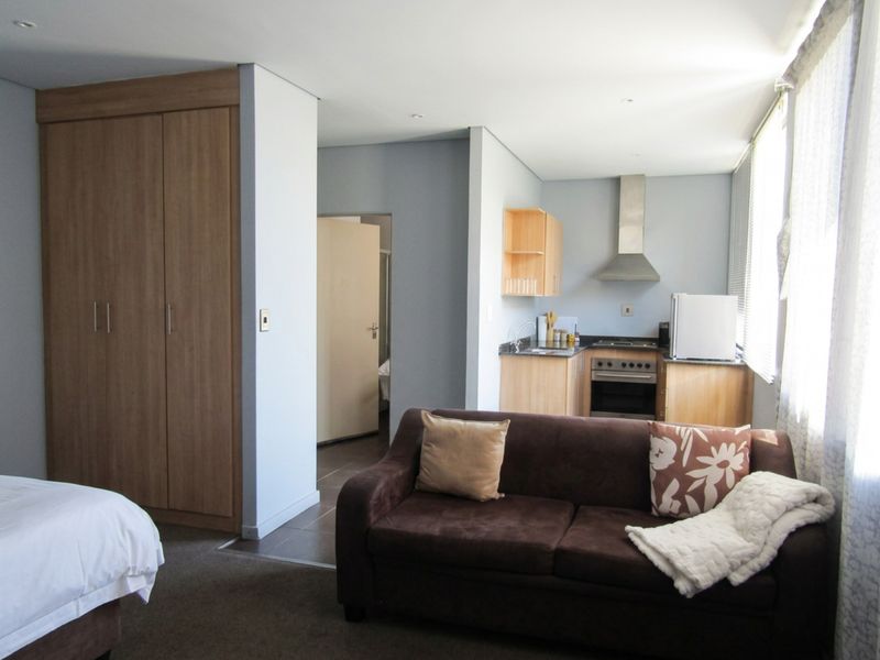 Open-plan studio apartment featuring a compact kitchen with built-in oven and hob, adjacent to a living area and built-in wardrobe storage.