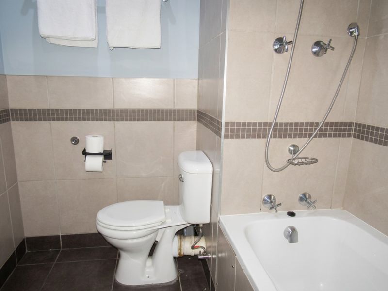 A functional bathroom featuring a standard toilet, bathtub with shower mixer, and neutral wall tiling with a decorative mosaic border.