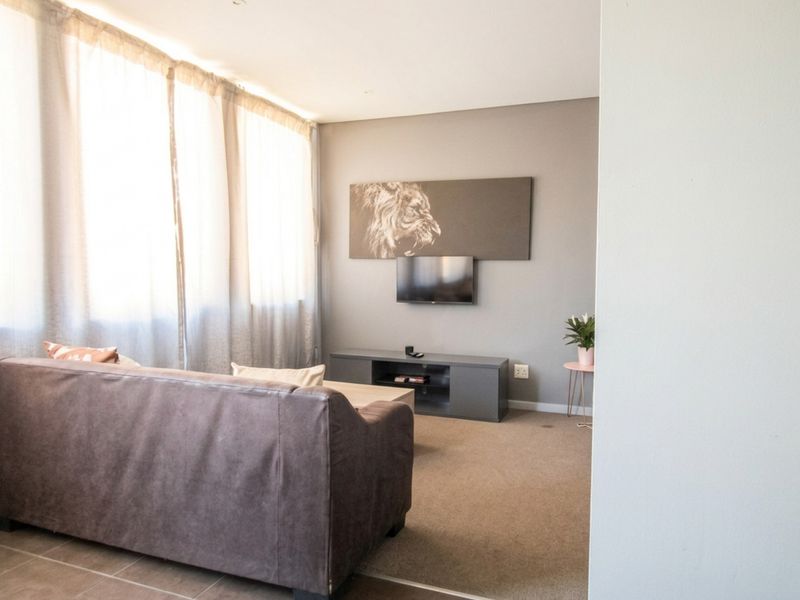 A comfortable living room featuring carpeted flooring, a large window with curtains, and a wall-mounted television setup.