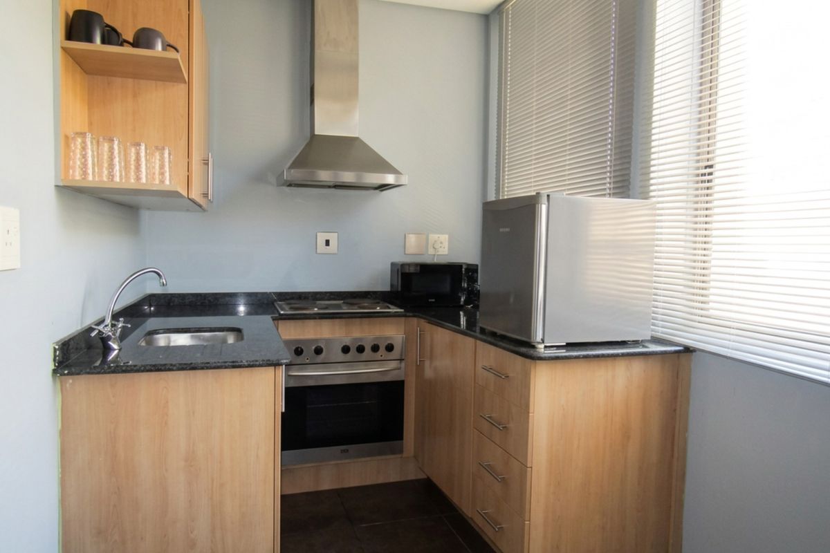 Compact kitchen featuring light wood cabinetry, granite countertops, stainless steel appliances including an oven, hob, and extractor fan, with natural light from large windows.