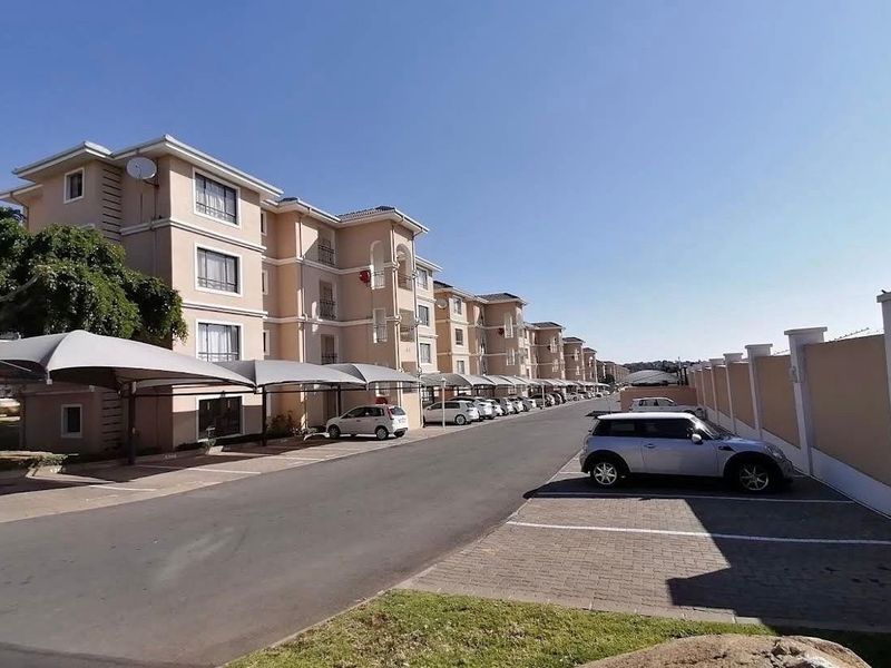 Exterior view of the apartment complex featuring paved driveways, covered parking bays, and secure perimeter walling.
