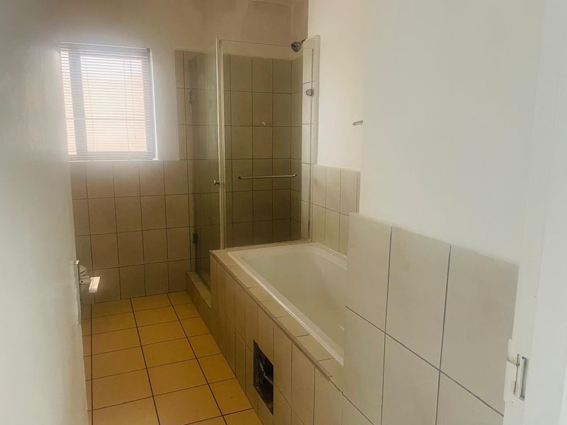 A functional bathroom featuring a built-in bathtub, separate shower enclosure, and neutral wall and floor tiling.