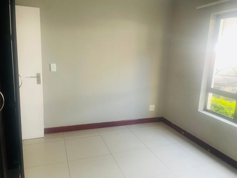 An empty bedroom featuring neutral wall paint, tiled flooring, and a window allowing natural light.
