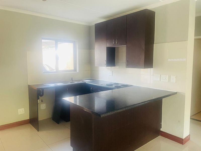 A functional kitchen featuring dark wood cabinetry, black granite countertops, a built-in electric hob, and a stainless steel sink with tiled backsplash.