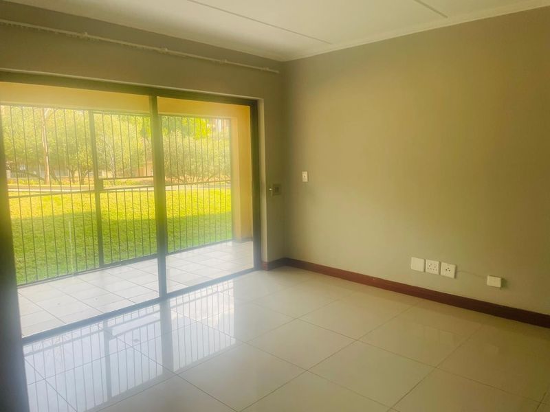 A bright, empty living room featuring neutral tiled floors, skirting boards, and a large sliding glass door providing access to an outdoor patio area.