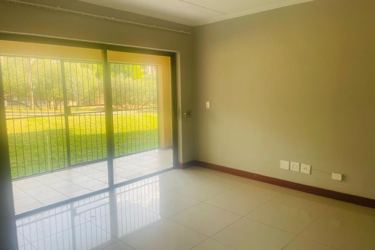 A bright, empty living room featuring neutral tiled floors, skirting boards, and a large sliding glass door providing access to an outdoor patio area.