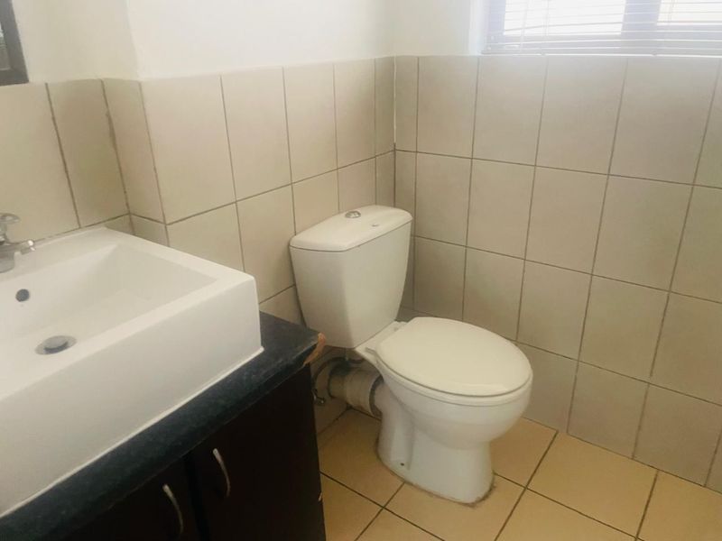 A functional bathroom featuring a vanity basin, toilet, and neutral wall and floor tiling.