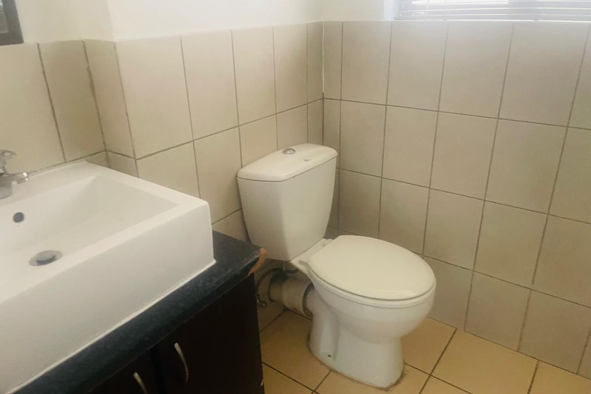 A functional bathroom featuring a vanity basin, toilet, and neutral wall and floor tiling.
