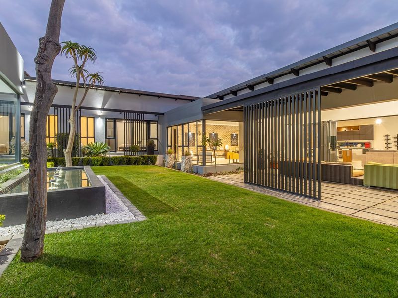 Modern rear courtyard featuring a manicured lawn, a contemporary water feature, and a covered patio area with integrated metal screening.