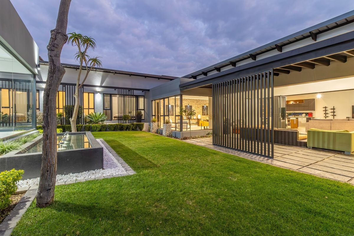 Modern rear courtyard featuring a manicured lawn, a contemporary water feature, and a covered patio area with integrated metal screening.