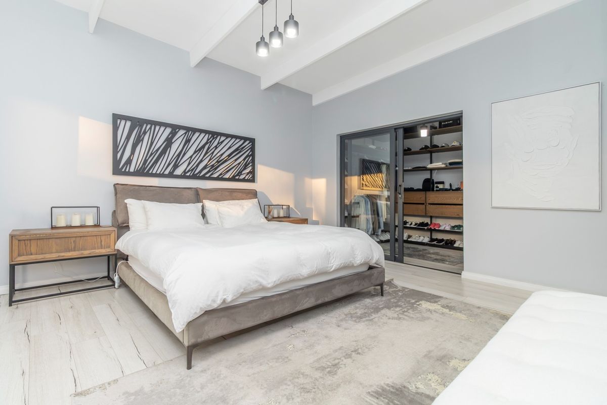 Spacious bedroom featuring vaulted ceilings with exposed beams, light-toned laminate flooring, and a modern walk-in closet with sliding glass doors.