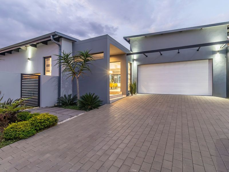 Modern front elevation featuring a paved driveway, double garage, and contemporary architectural design with integrated exterior lighting.