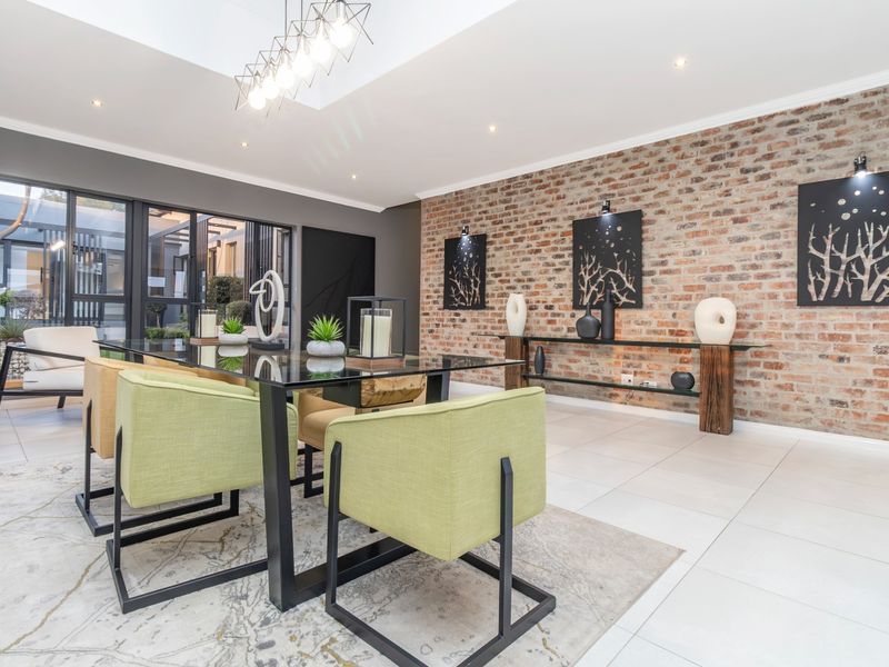 Modern dining room featuring an exposed brick wall, large glass sliding doors, tiled flooring, and a bright skylight, creating an elegant and airy atmosphere.