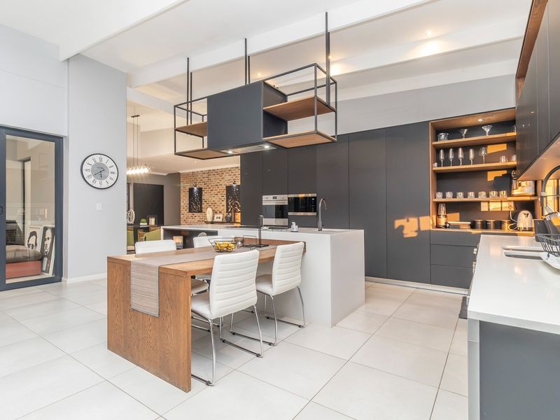 Modern open-plan kitchen featuring sleek dark cabinetry, a central island with integrated dining, stone countertops, and exposed ceiling beams, flowing into the living area.