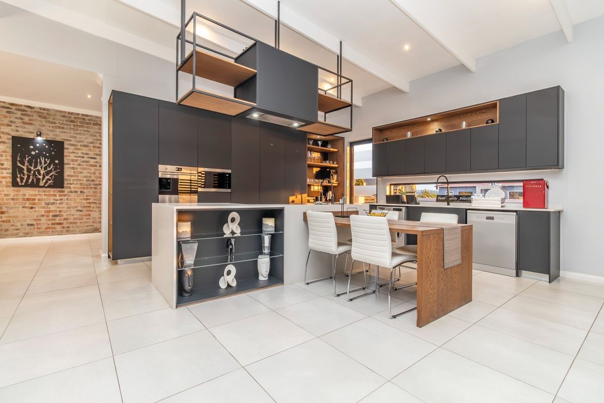 Modern kitchen featuring dark cabinetry, a central island with integrated seating, built-in appliances, and an exposed brick feature wall.