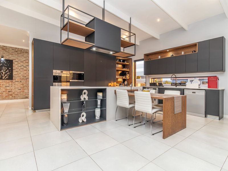 Modern kitchen featuring dark cabinetry, a central island with integrated seating, built-in appliances, and an exposed brick feature wall.