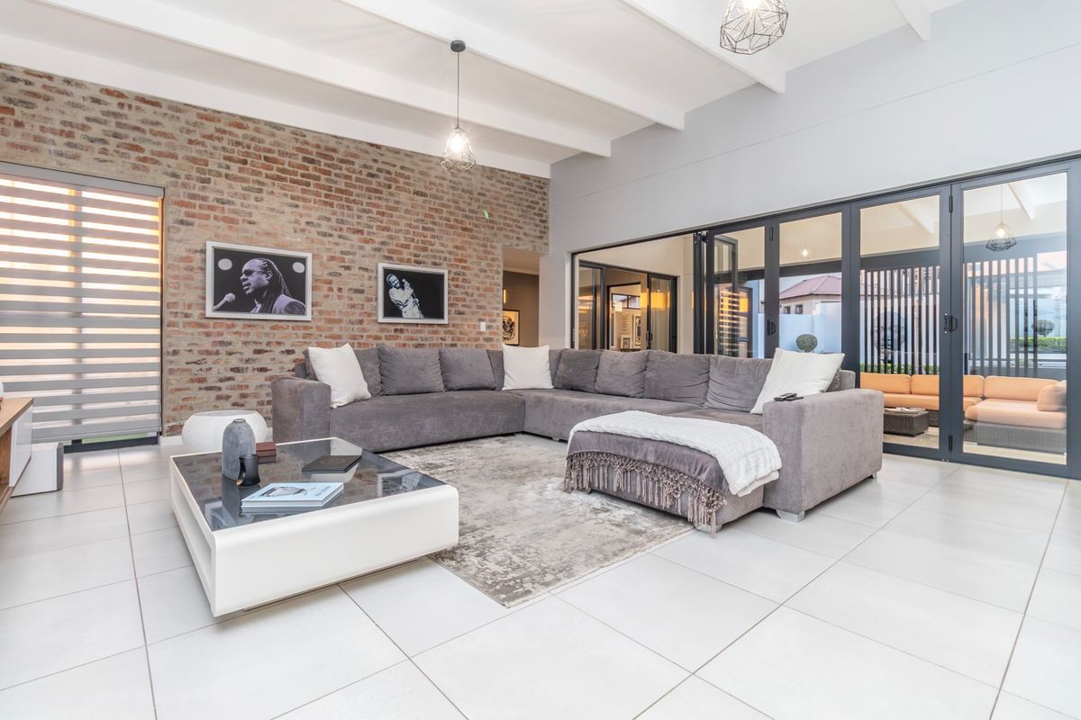 Spacious living room featuring an exposed brick feature wall, vaulted ceilings with exposed beams, large format floor tiles, and modern aluminium stacker doors.