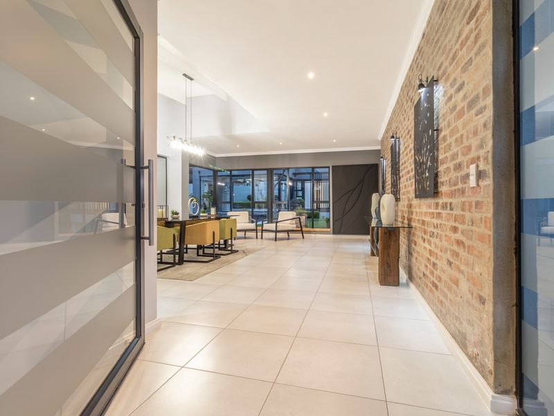 Spacious open-plan living area featuring a striking exposed brick feature wall, large format floor tiles, and expansive glass doors leading to the outdoor space.