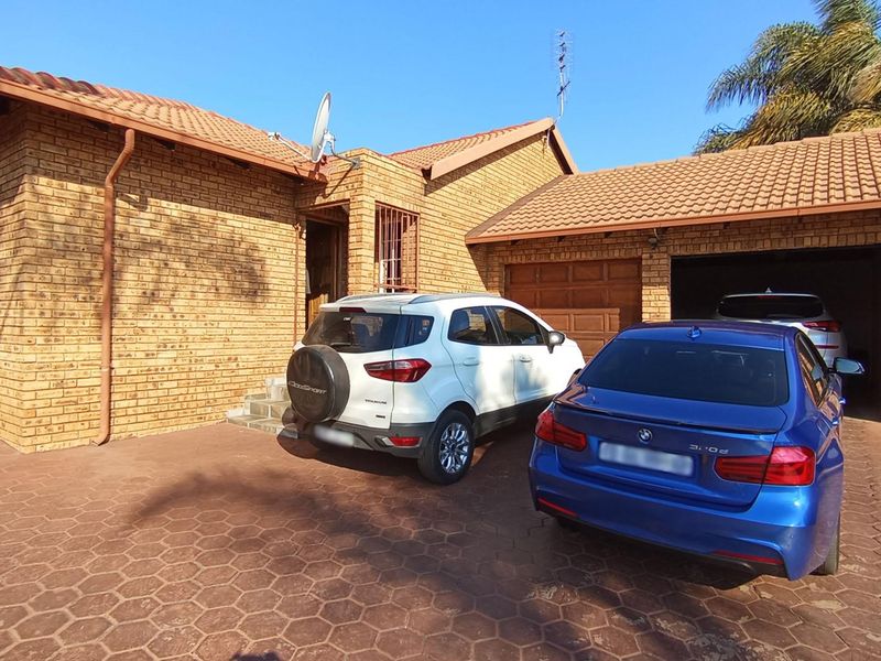 Front elevation of a face brick townhouse featuring a double garage, paved driveway, and tiled roof with solar panel installation.